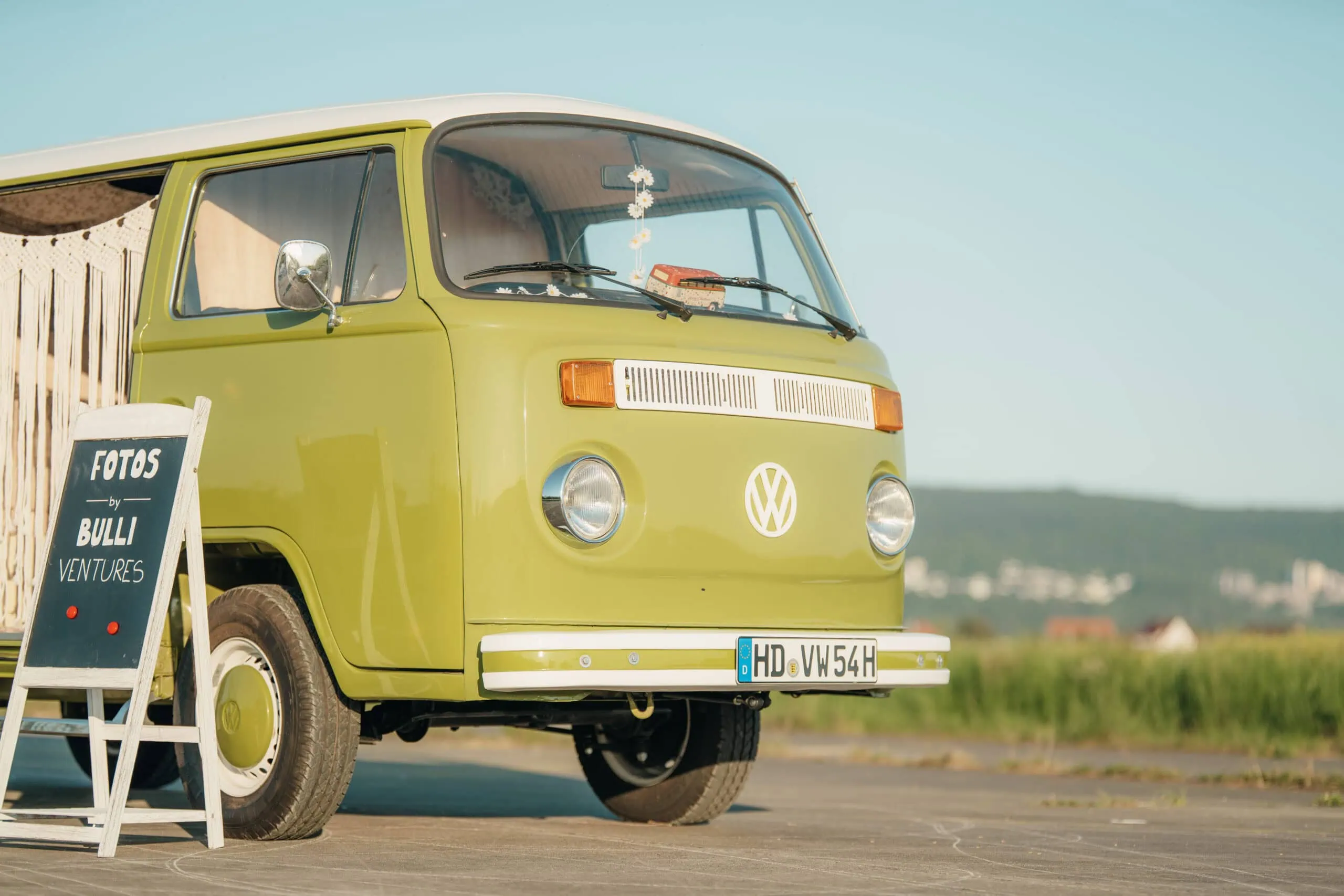 Grüner VW-Oldtimer-Bus neben einem Schild mit der Aufschrift FOTOS BULLI VENTURES.