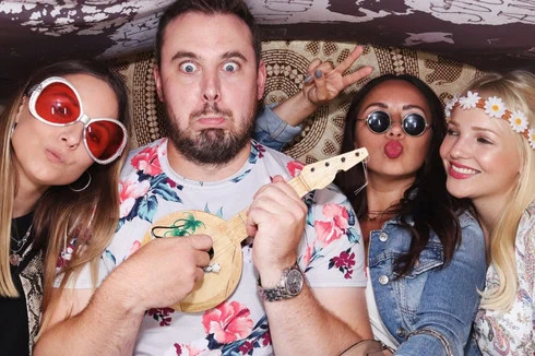 Vier Erwachsene posieren verspielt - ein Mann mit kleiner Gitarre, drei Frauen mit Sonnenbrillen.